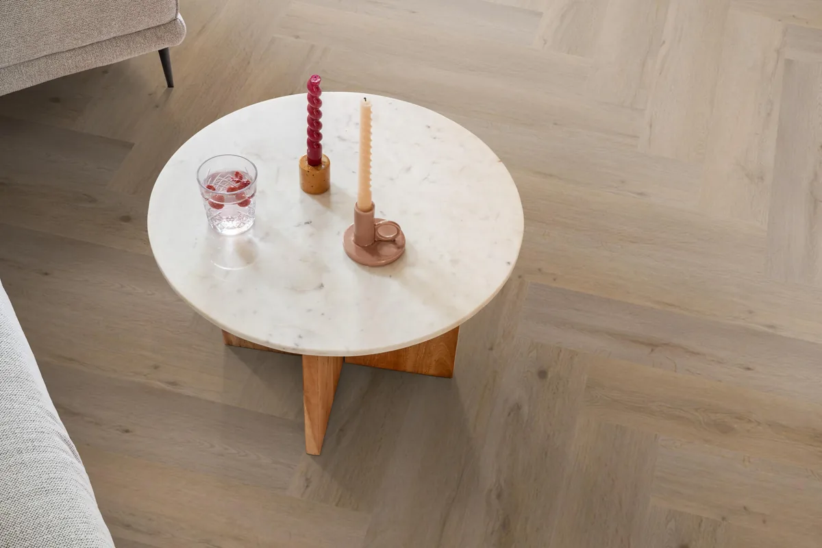 Leyton / Vivero natural oak, visgraat plak pvc in een woonkamer, met een ronde marmeren salontafel en twee kaarsen