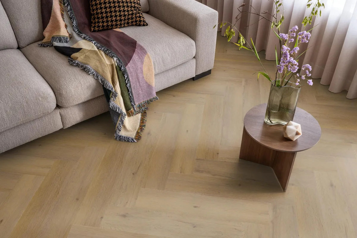 Leyton / Vivero dark oak, visgraat plak pvc in een woonkamer, met een beige bank en een ronde bijzettafel met bloemen