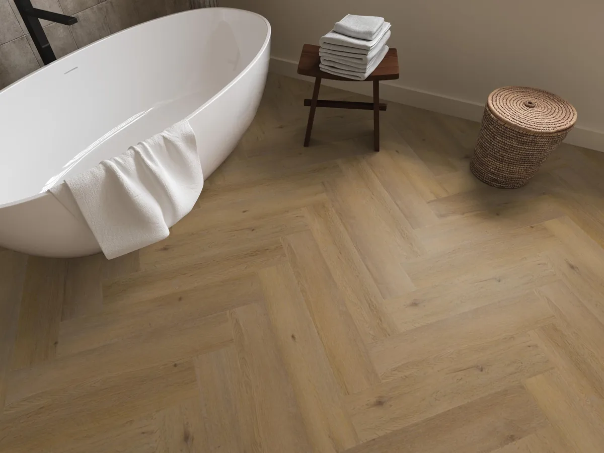 Leyton / Vivero dark oak, visgraat plak pvc in een badkamer, met een vrijstaand bad en een rieten wasmand
