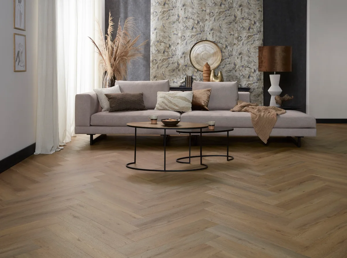Leyton / Vivero dark oak, visgraat plak pvc in een woonkamer met een stenen wand, een lichtgrijze bank en twee ronde bijzettafels