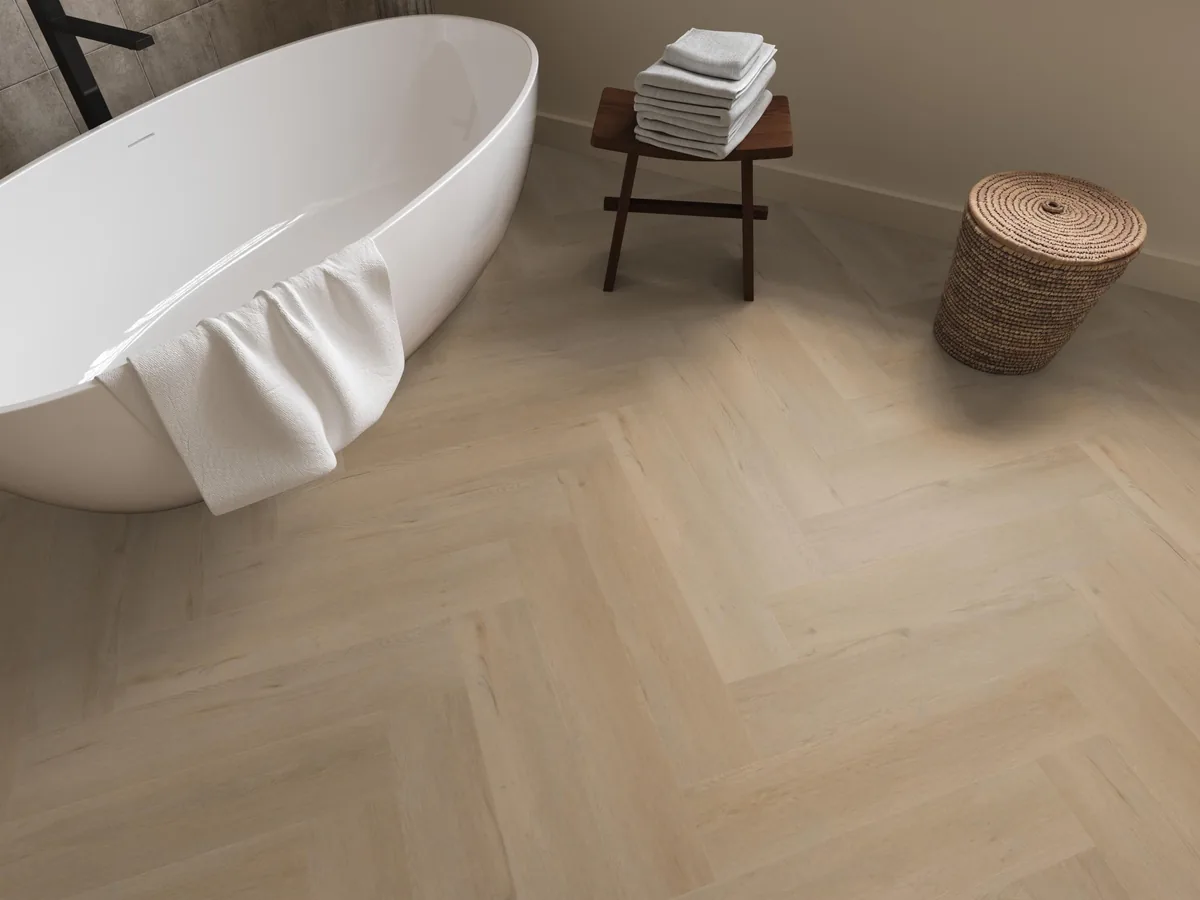Leyton / Vivero beige, visgraat plak pvc in een badkamer, met een vrijstaand bad en een rieten wasmand