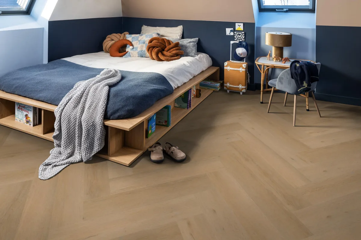 Leyton / Vivero warm oak, visgraat plak pvc in een slaapkamer onder een schuin dak, met een houten bedombouw en sloffen ervoor