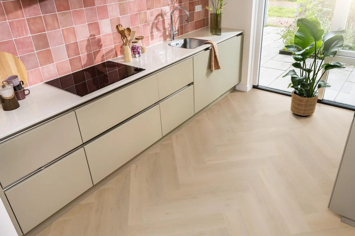 Leyton / Vivero warm oak, visgraat plak pvc in een keuken met een roze tegelwand en openslaande tuindeuren