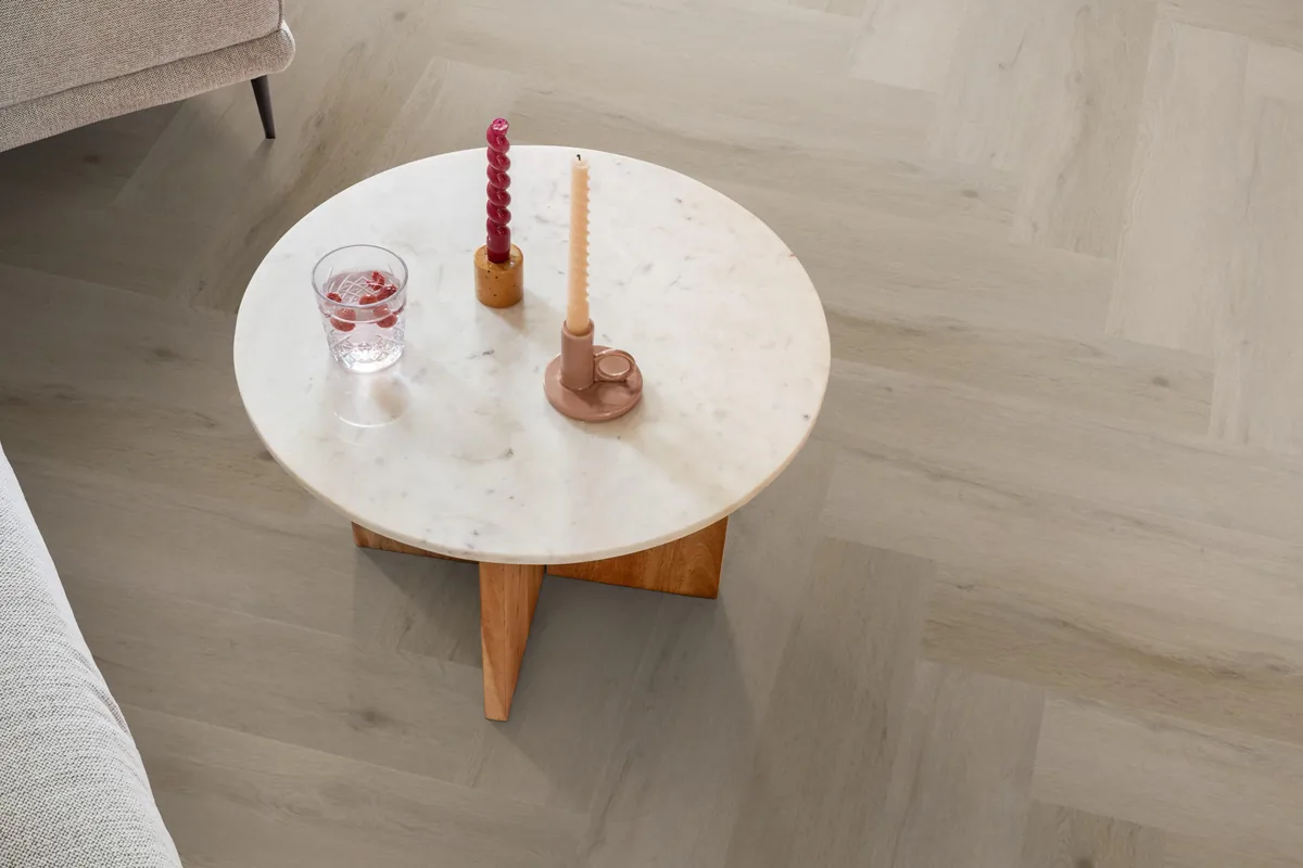 Leyton / Vivero Light oak, visgraat klik pvc in een woonkamer, met een ronde marmeren salontafel en twee kaarsen