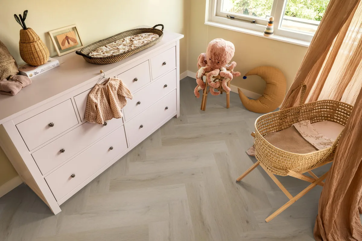 Leyton / Vivero Light oak, visgraat klik pvc in een babykamer, met een witte commode en een rieten wieg