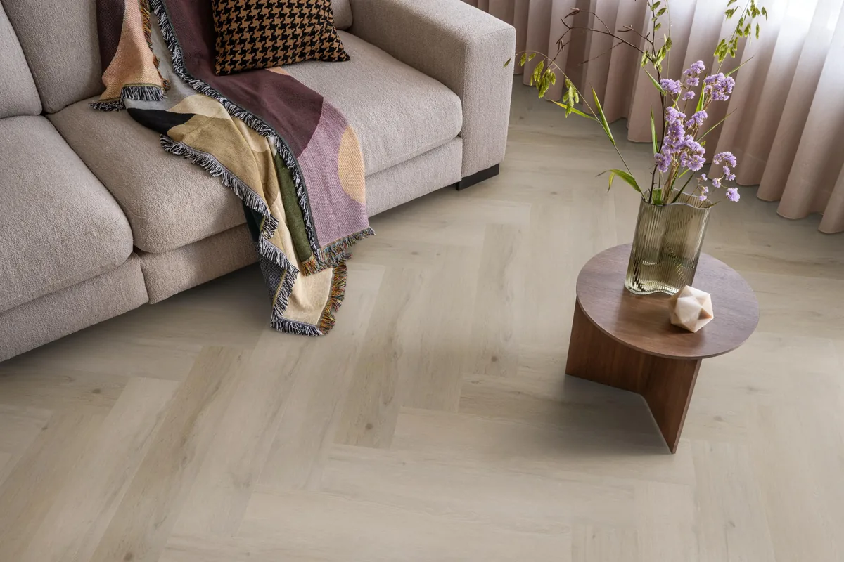 Leyton / Vivero Light oak, visgraat klik pvc in een woonkamer, met een beige bank en een ronde bijzettafel met bloemen