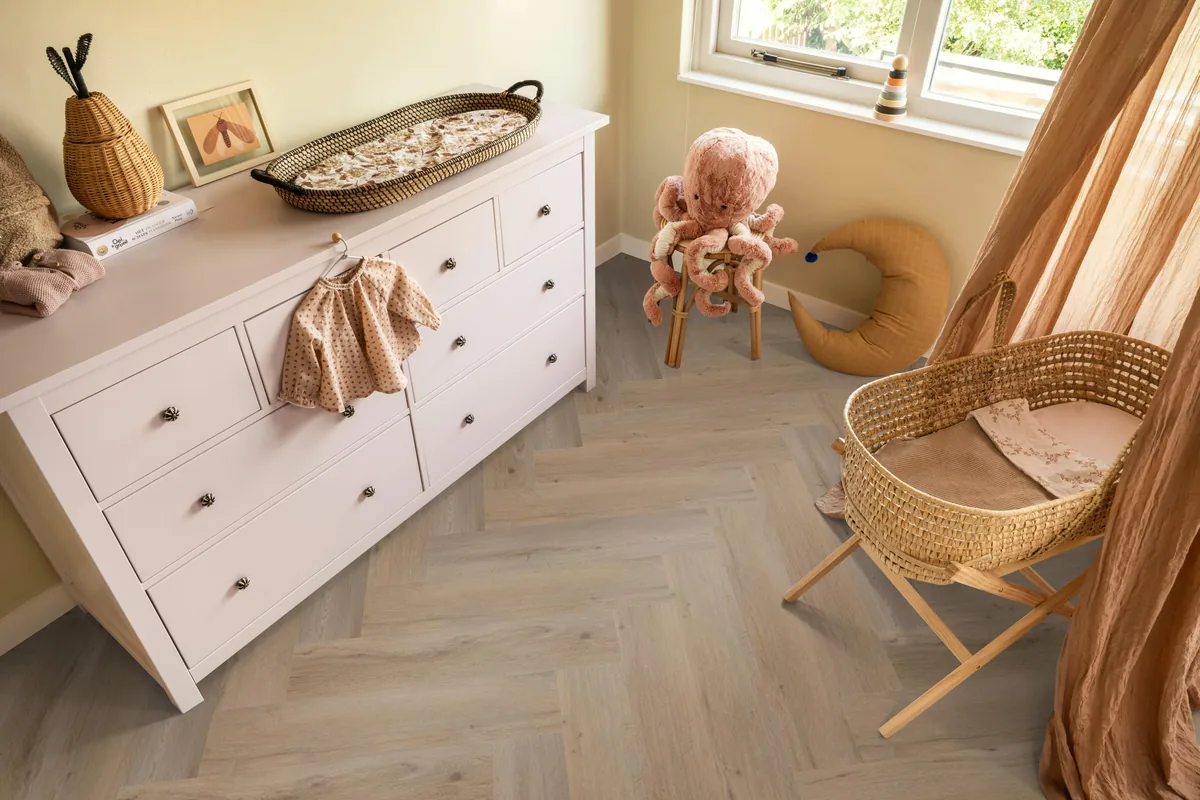 Leyton / Vivero Smoky, visgraat klik pvc in een babykamer, met een witte commode en een rieten wieg
