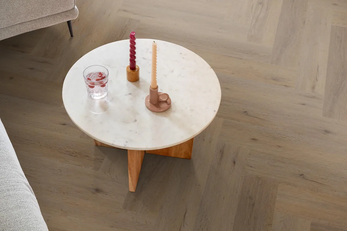 Leyton / Vivero Natural oak, visgraat klik pvc in een woonkamer, met een ronde marmeren salontafel en twee kaarsen