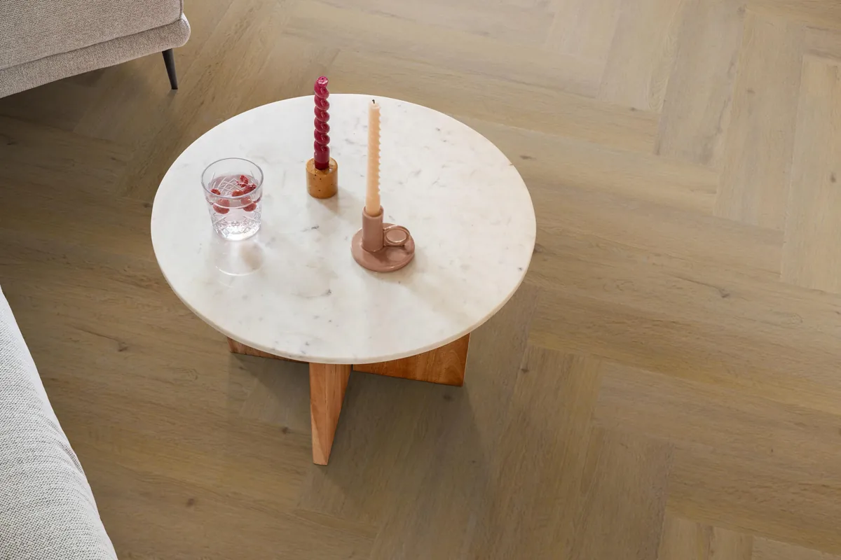 Leyton / Vivero Dark oak, visgraat klik pvc in een woonkamer, met een ronde marmeren salontafel en twee kaarsen