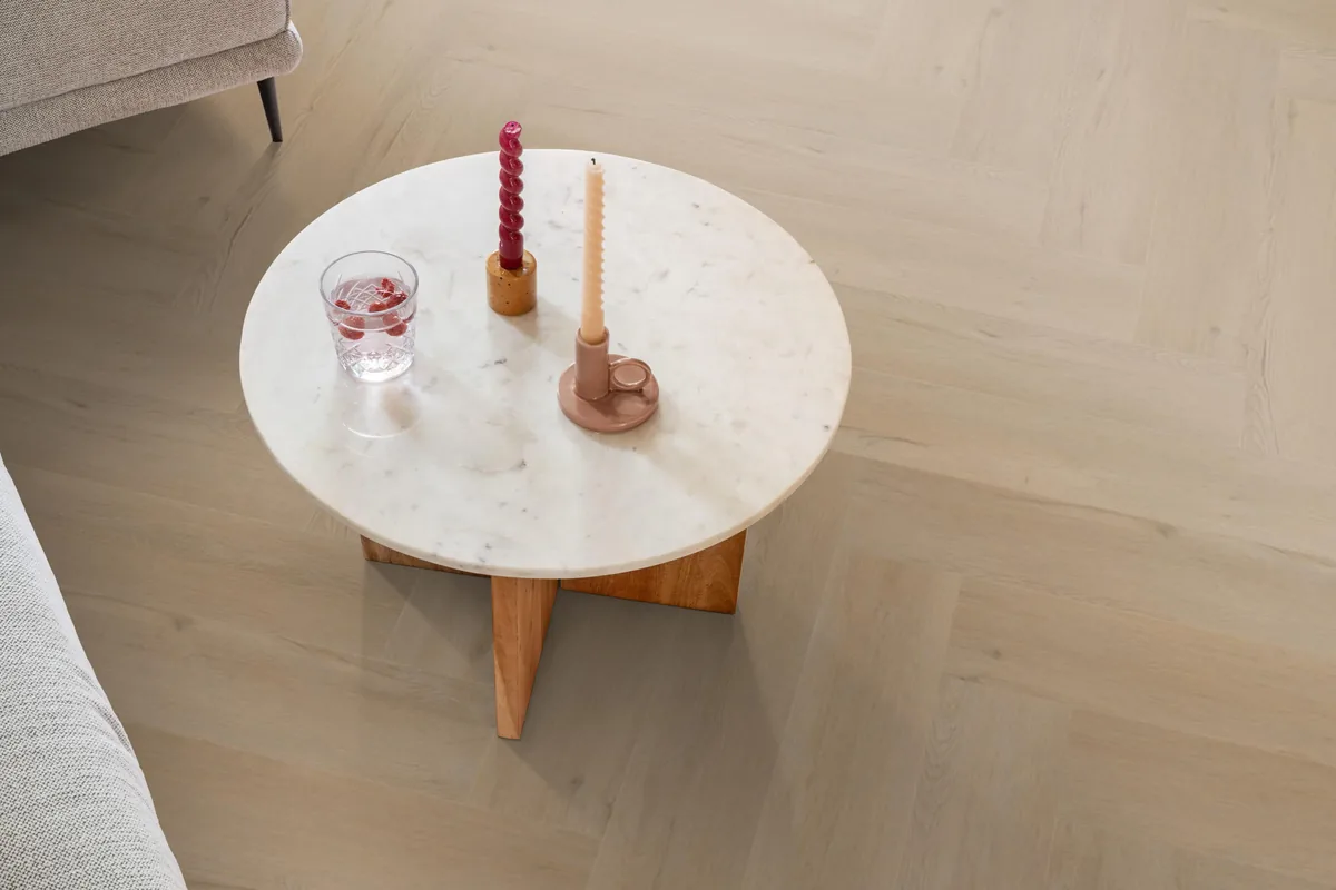 Leyton / Vivero Beige, visgraat klik pvc in een woonkamer, met een ronde marmeren salontafel en twee kaarsen
