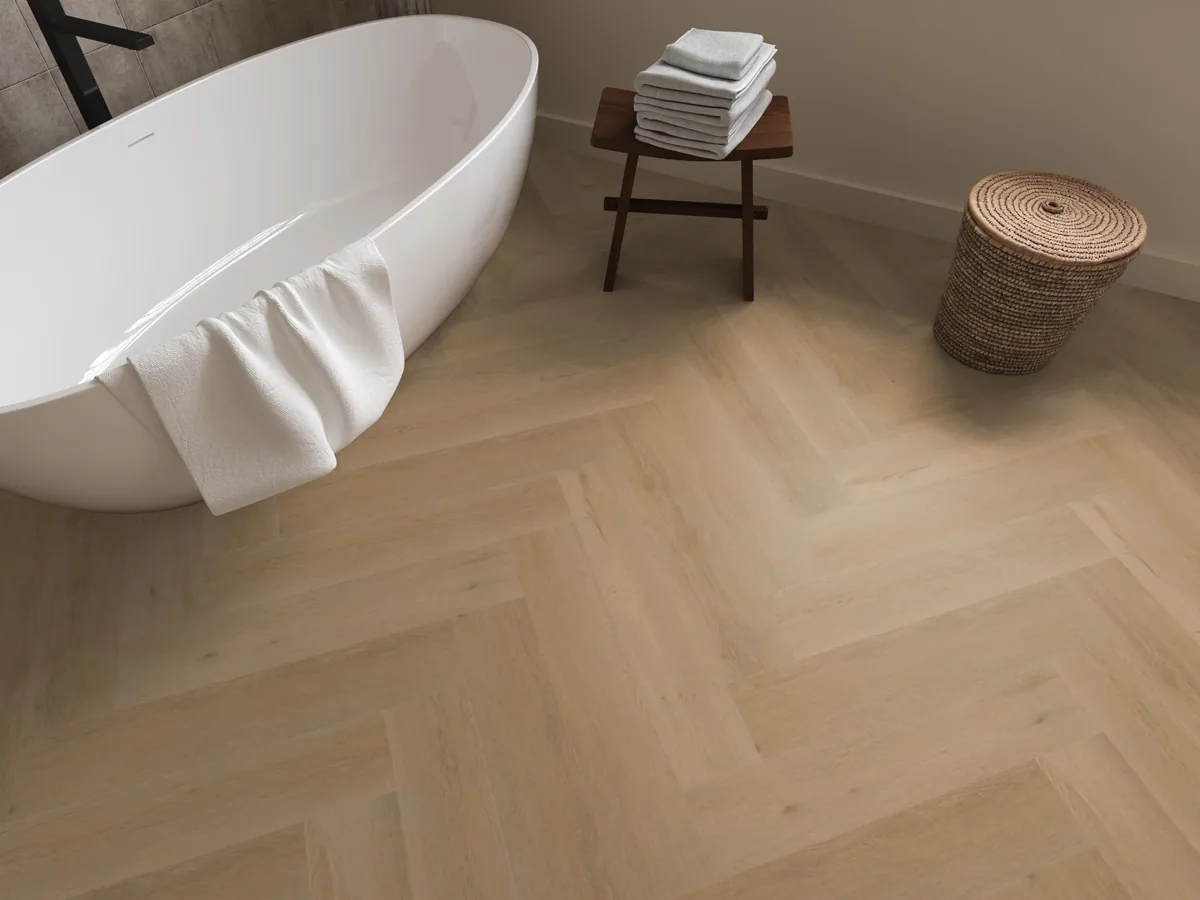 Leyton / Vivero Warm oak, visgraat klik pvc in een badkamer, met een vrijstaand bad en een rieten wasmand