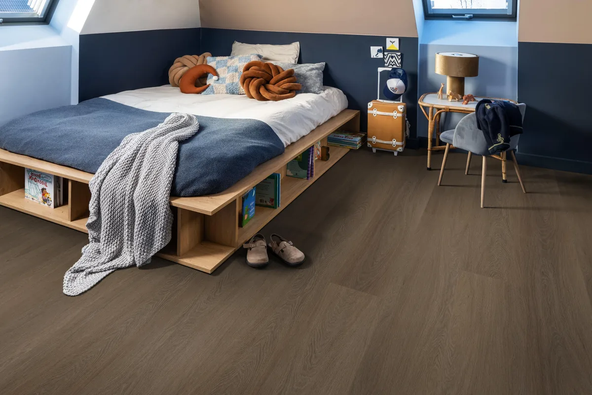 Fulham / Estino brown, plak pvc in een slaapkamer onder een schuin dak, met een houten bedombouw en sloffen ervoor