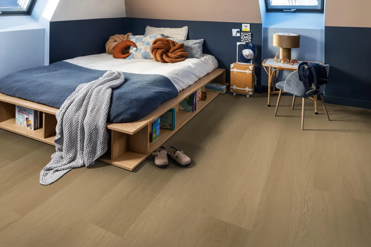 Fulham / Estino warm oak, klik pvc in een slaapkamer onder een schuin dak, met een houten bedombouw en sloffen ervoor