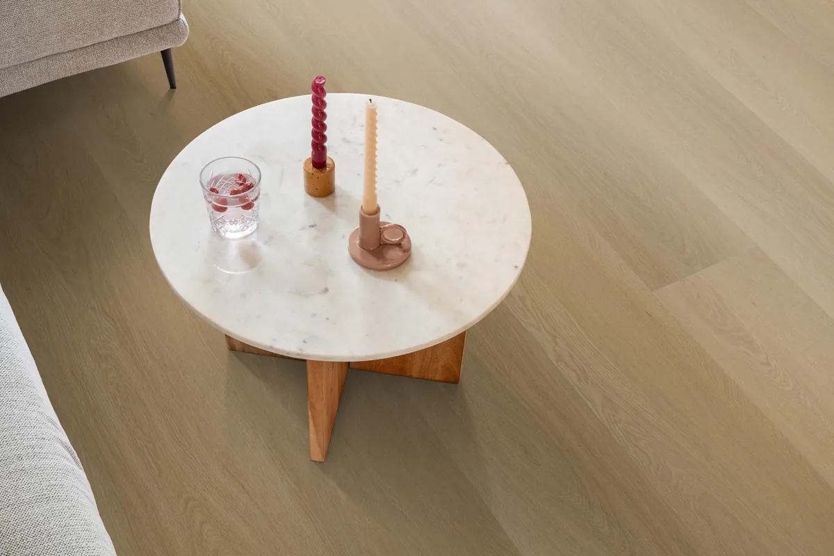 Fulham / Estino warm oak, klik pvc in een woonkamer, met een ronde marmeren salontafel en twee kaarsen
