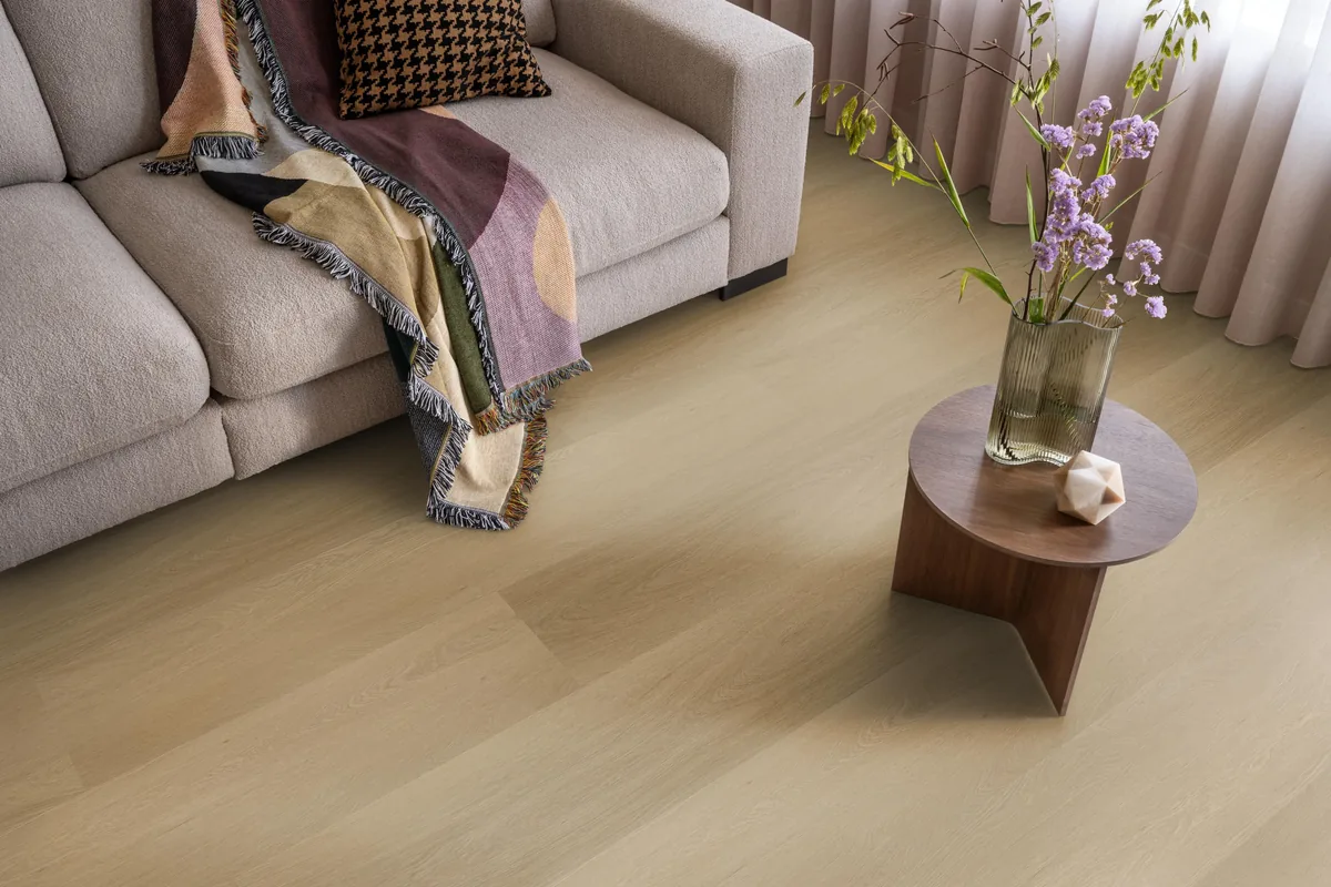 Fulham / Estino warm oak, klik pvc in een woonkamer, met een beige bank en een ronde bijzettafel met bloemen