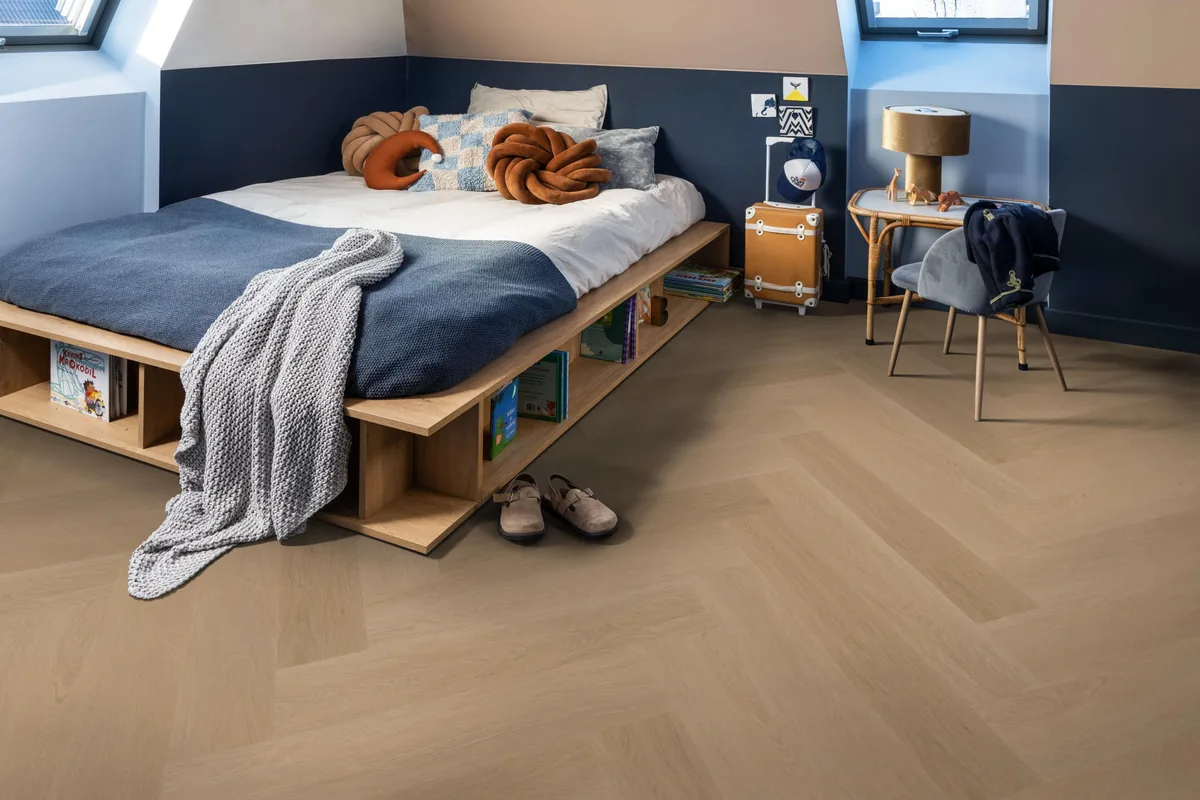 Fulham / Estino dark oak, visgraat plak pvc in een slaapkamer onder een schuin dak, met een houten bedombouw en sloffen ervoor