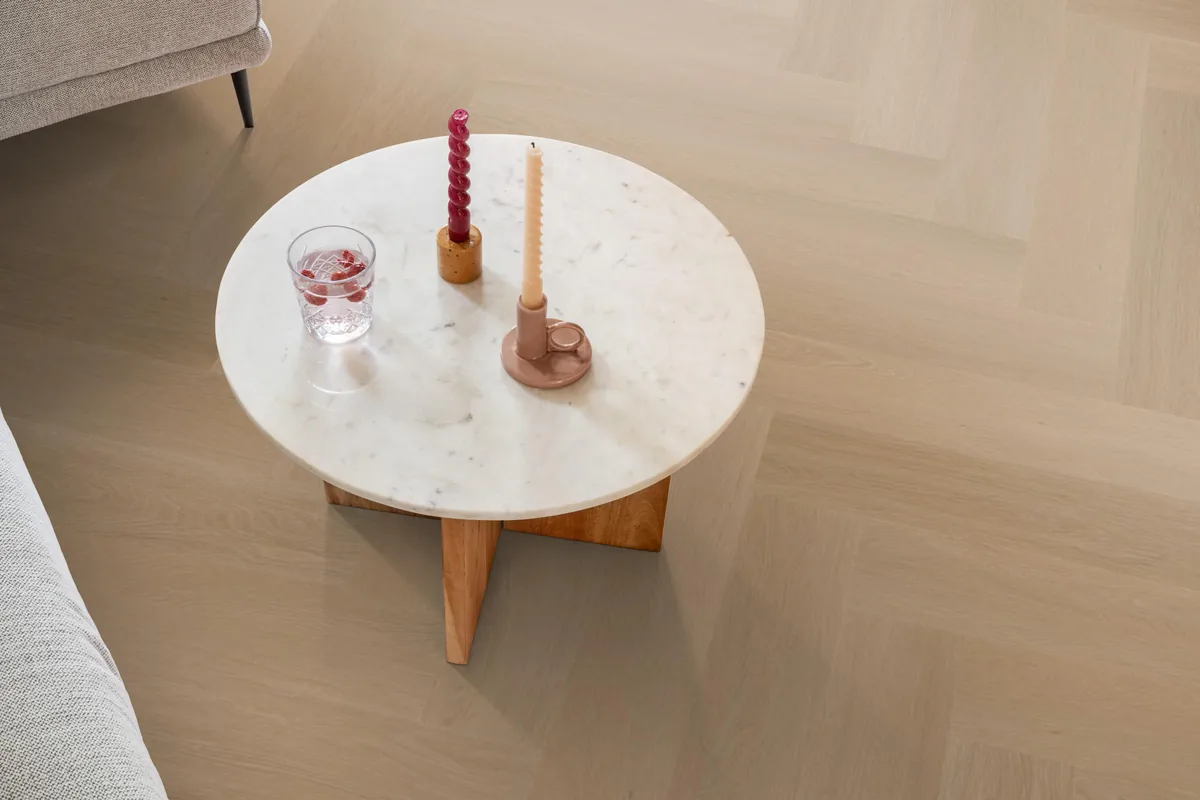 Fulham / Estino dark oak, visgraat plak pvc in een woonkamer, met een ronde marmeren salontafel en twee kaarsen