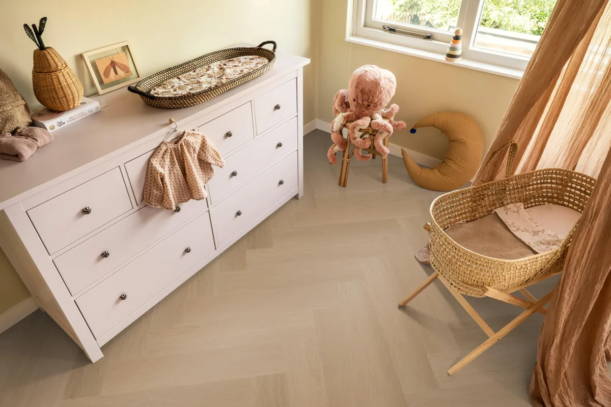 Fulham / Estino dark oak, visgraat plak pvc in een babykamer, met een witte commode en een rieten wieg