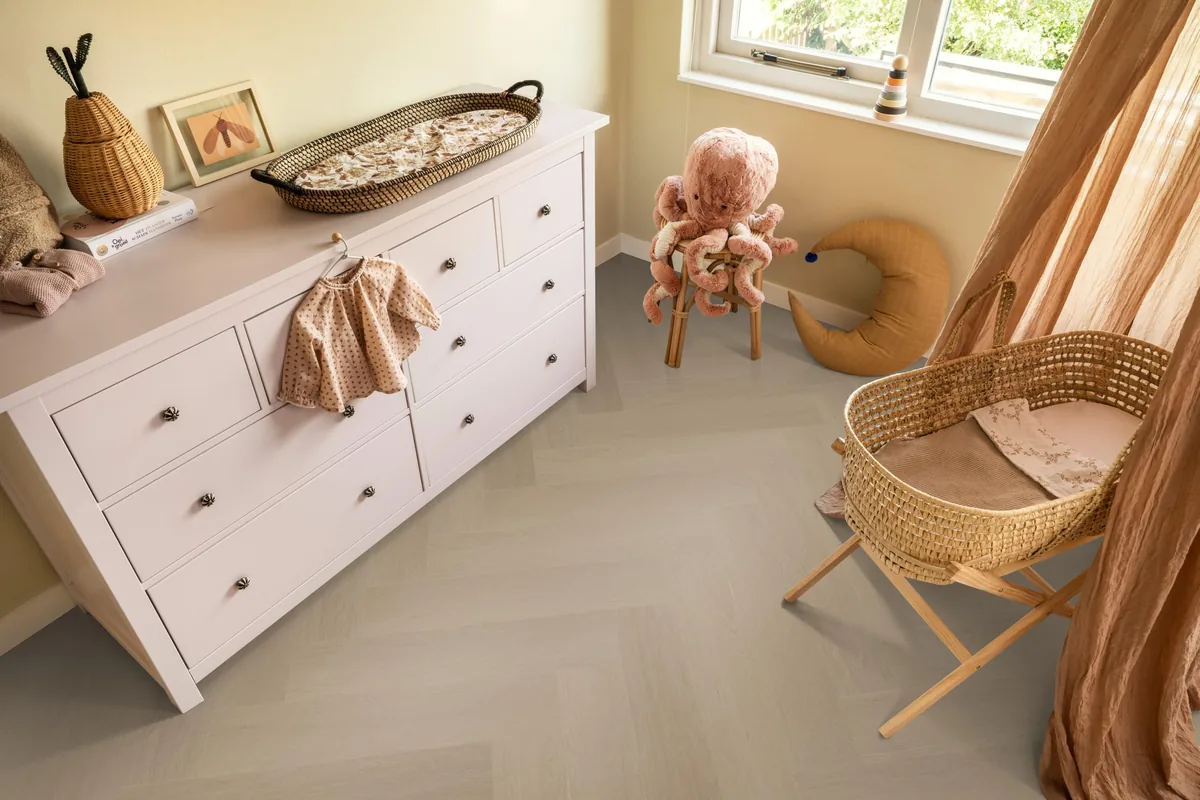 Fulham / Estino smoky, visgraat plak pvc in een babykamer, met een witte commode en een rieten wieg