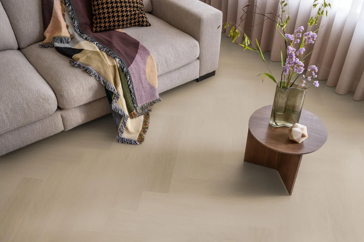 Fulham / Estino smoky, visgraat plak pvc in een woonkamer, met een beige bank en een ronde bijzettafel met bloemen