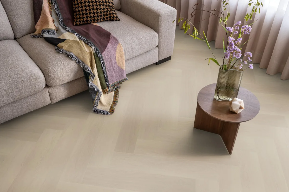 Fulham / Estino beige, visgraat plak pvc in een woonkamer, met een beige bank en een ronde bijzettafel met bloemen