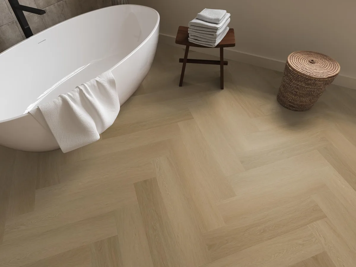 Fulham / Estino warm oak, visgraat plak pvc in een badkamer, met een vrijstaand bad en een rieten wasmand