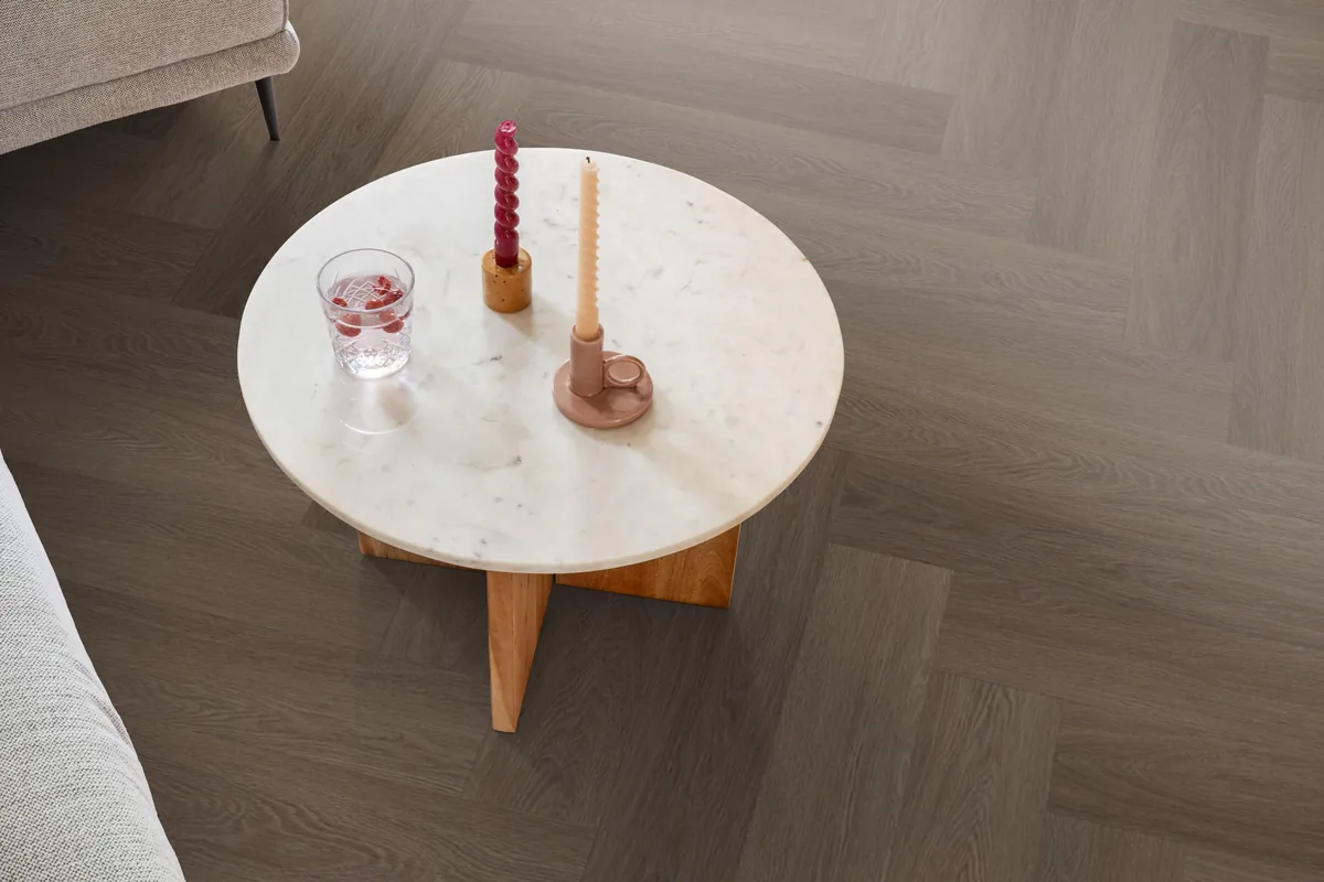 Fulham / Estino brown, visgraat plak pvc in een woonkamer, met een ronde marmeren salontafel en twee kaarsen