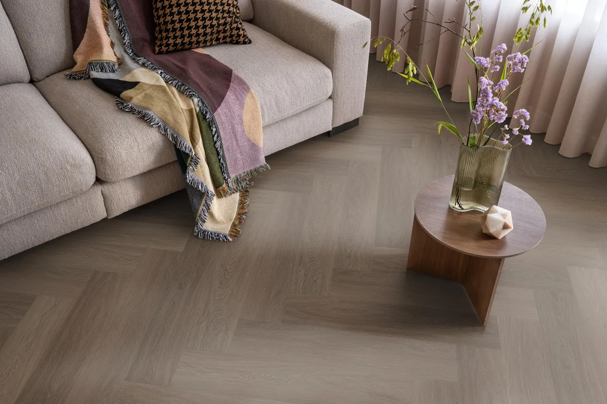 Fulham / Estino brown, visgraat plak pvc in een woonkamer, met een beige bank en een ronde bijzettafel met bloemen