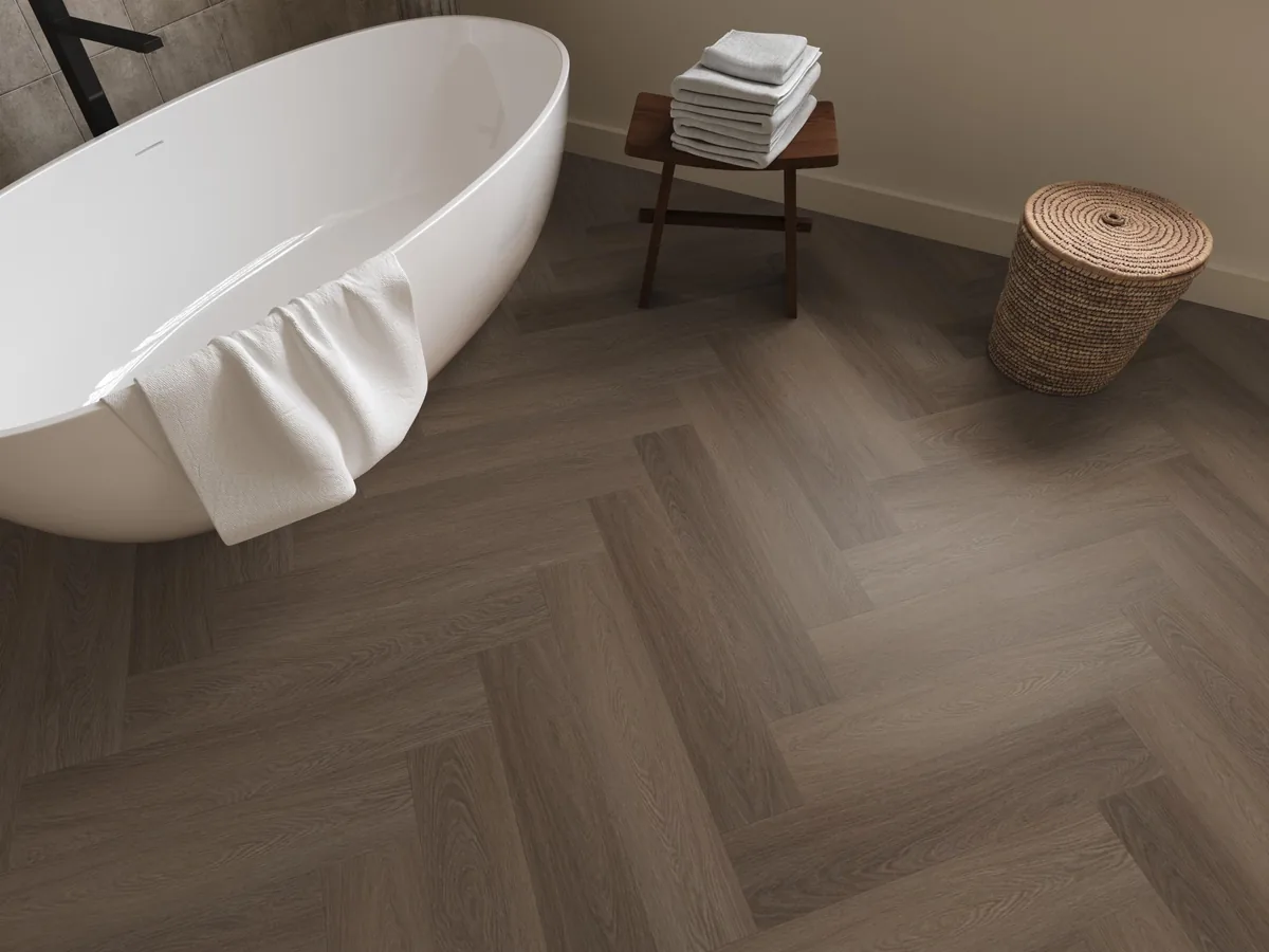Fulham / Estino brown, visgraat plak pvc in een badkamer, met een vrijstaand bad en een rieten wasmand