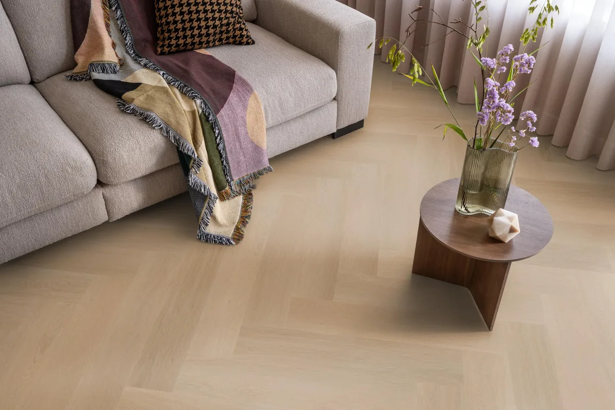 Fulham / Estino Dark oak, visgraat klik pvc in een woonkamer, met een beige bank en een ronde bijzettafel met bloemen