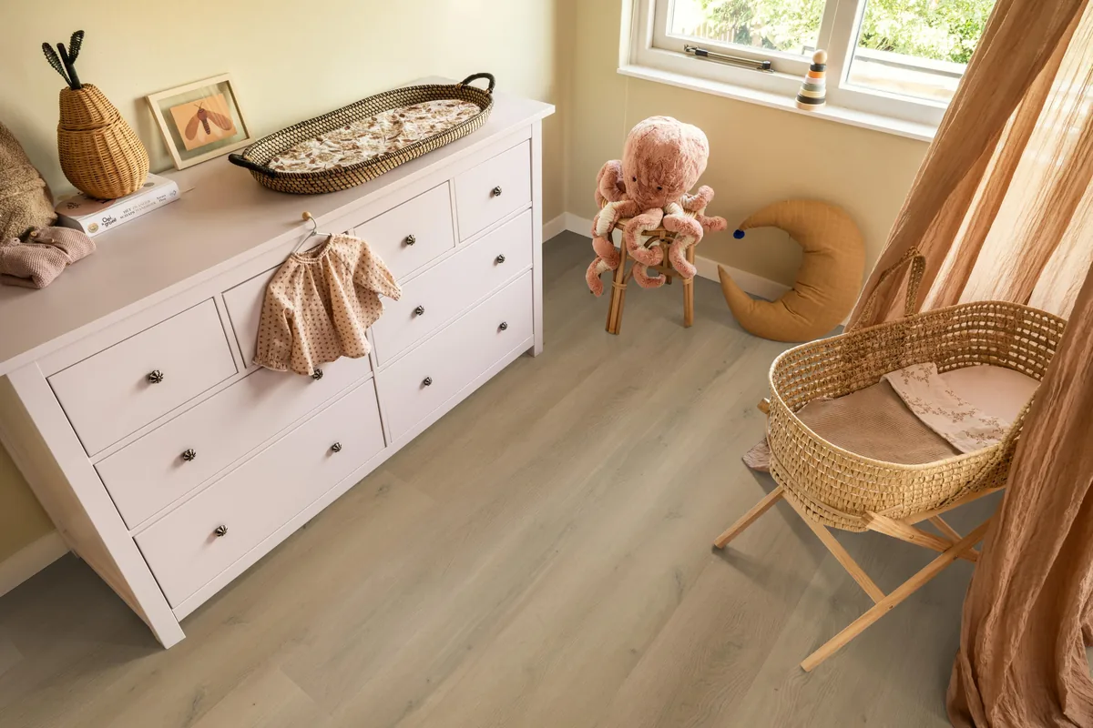 Greenwich / Espero warm oak, plak pvc in een babykamer, met een witte commode en een rieten wieg