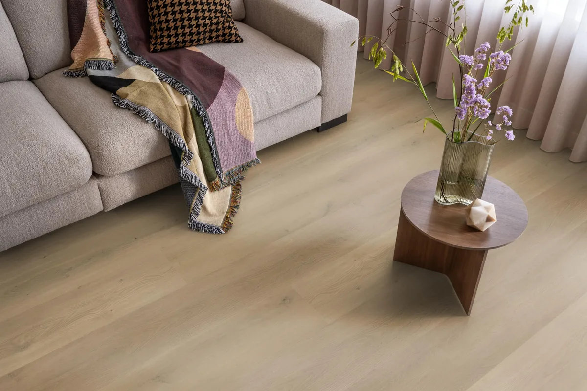 Greenwich / Espero warm oak, plak pvc in een woonkamer, met een beige bank en een ronde bijzettafel met bloemen
