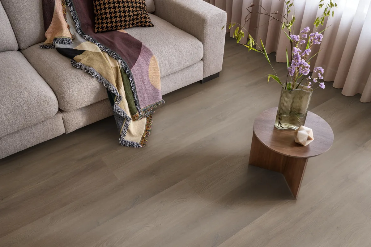 Greenwich / Espero warm brown, plak pvc in een woonkamer, met een beige bank en een ronde bijzettafel met bloemen