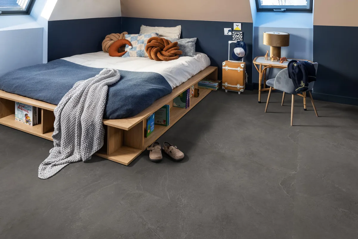 Stanmore / Noveno dark grey, plak pvc in een slaapkamer onder een schuin dak, met een houten bedombouw en sloffen ervoor