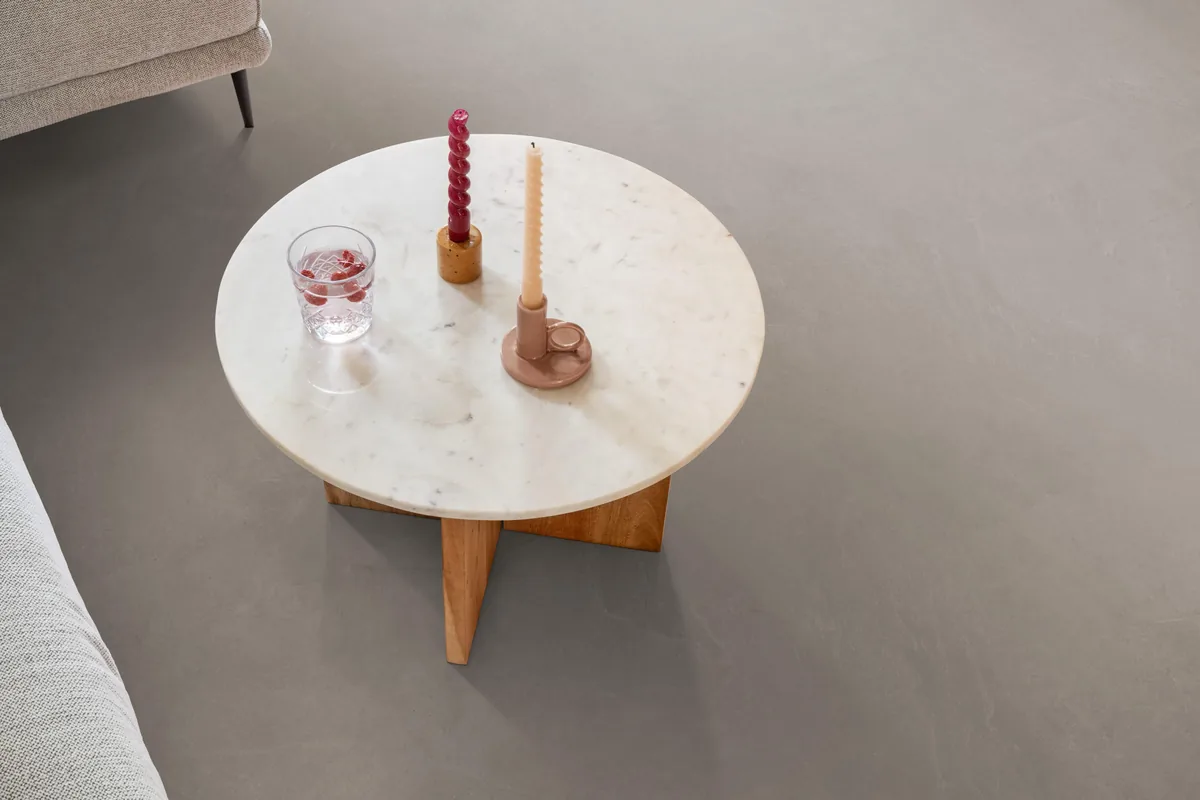 Stanmore / Noveno warm grey, klik pvc in een woonkamer, met een ronde marmeren salontafel en twee kaarsen