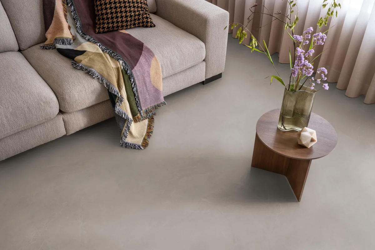 Stanmore / Noveno warm grey, klik pvc in een woonkamer, met een beige bank en een ronde bijzettafel met bloemen