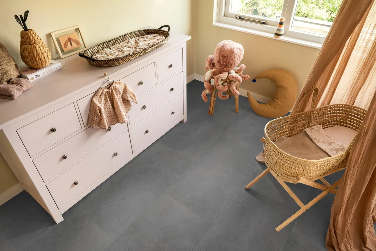 Southwark / Sarino dark grey, klik pvc in een babykamer, met een witte commode en een rieten wieg