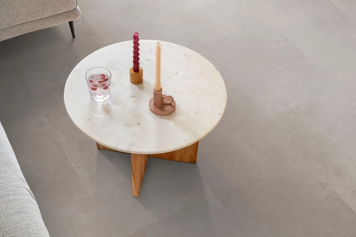 Southwark / Sarino light grey, klik pvc in een woonkamer, met een ronde marmeren salontafel en twee kaarsen