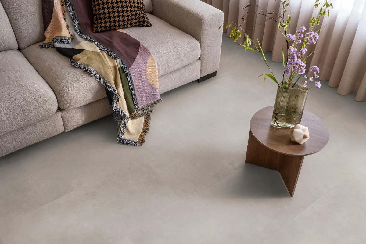 Southwark / Sarino light grey, klik pvc in een woonkamer, met een beige bank en een ronde bijzettafel met bloemen