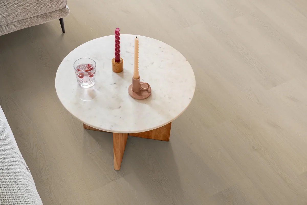 Merton / Navaro beige, plak pvc in een woonkamer, met een ronde marmeren salontafel en twee kaarsen