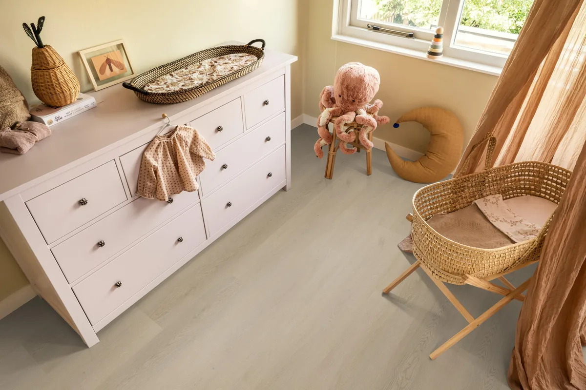 Merton / Navaro beige, plak pvc in een babykamer, met een witte commode en een rieten wieg