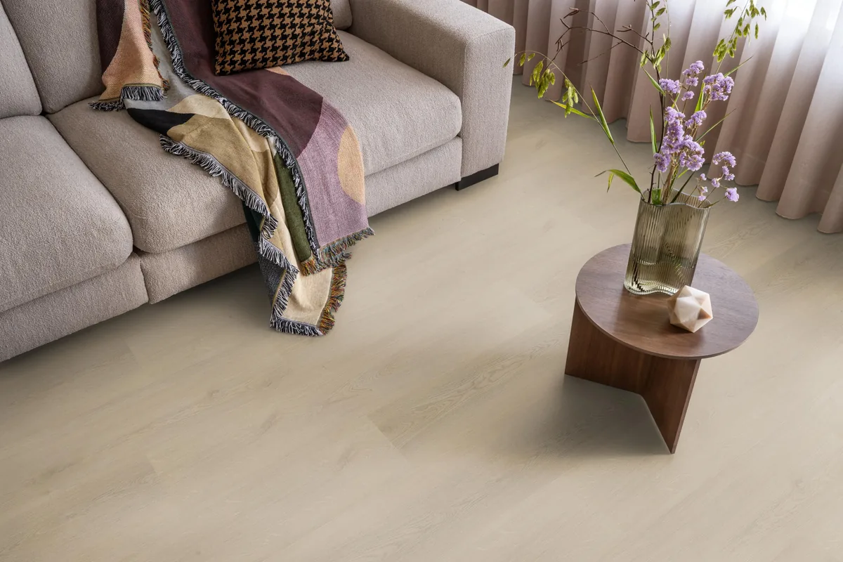 Merton / Navaro beige, plak pvc in een woonkamer, met een beige bank en een ronde bijzettafel met bloemen