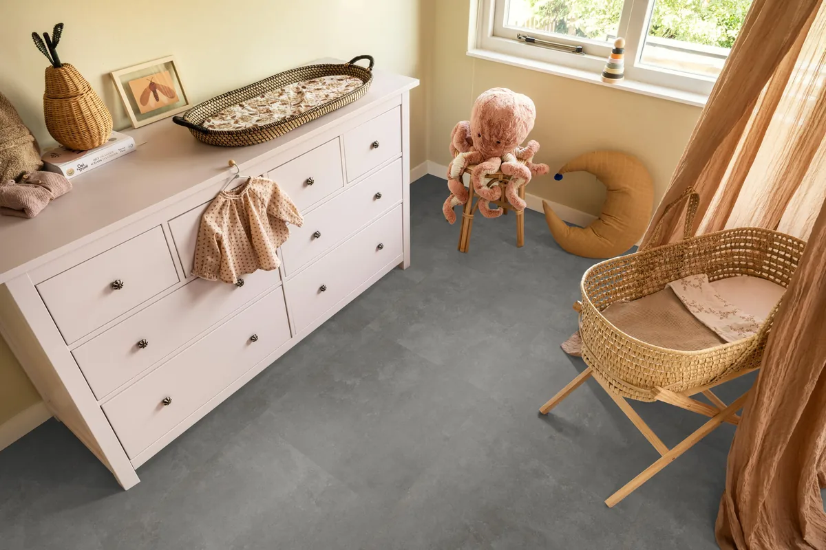 Victoria / Ceramo grey, klik pvc in een babykamer, met een witte commode en een rieten wieg