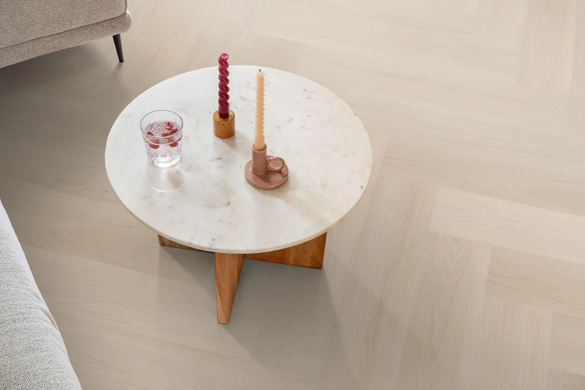 Brentford / Soleno Beige, visgraat klik pvc in een woonkamer, met een ronde marmeren salontafel en twee kaarsen
