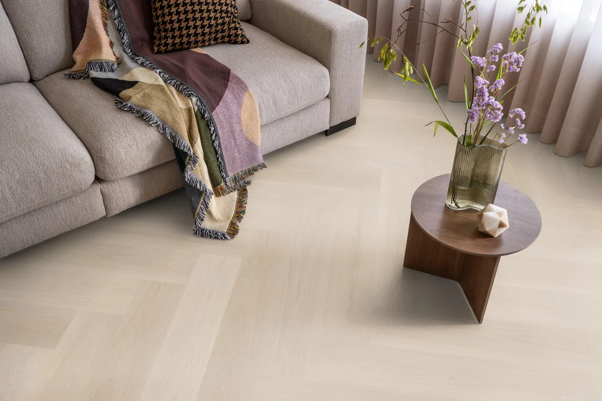 Brentford / Soleno Beige, visgraat klik pvc in een woonkamer, met een beige bank en een ronde bijzettafel met bloemen