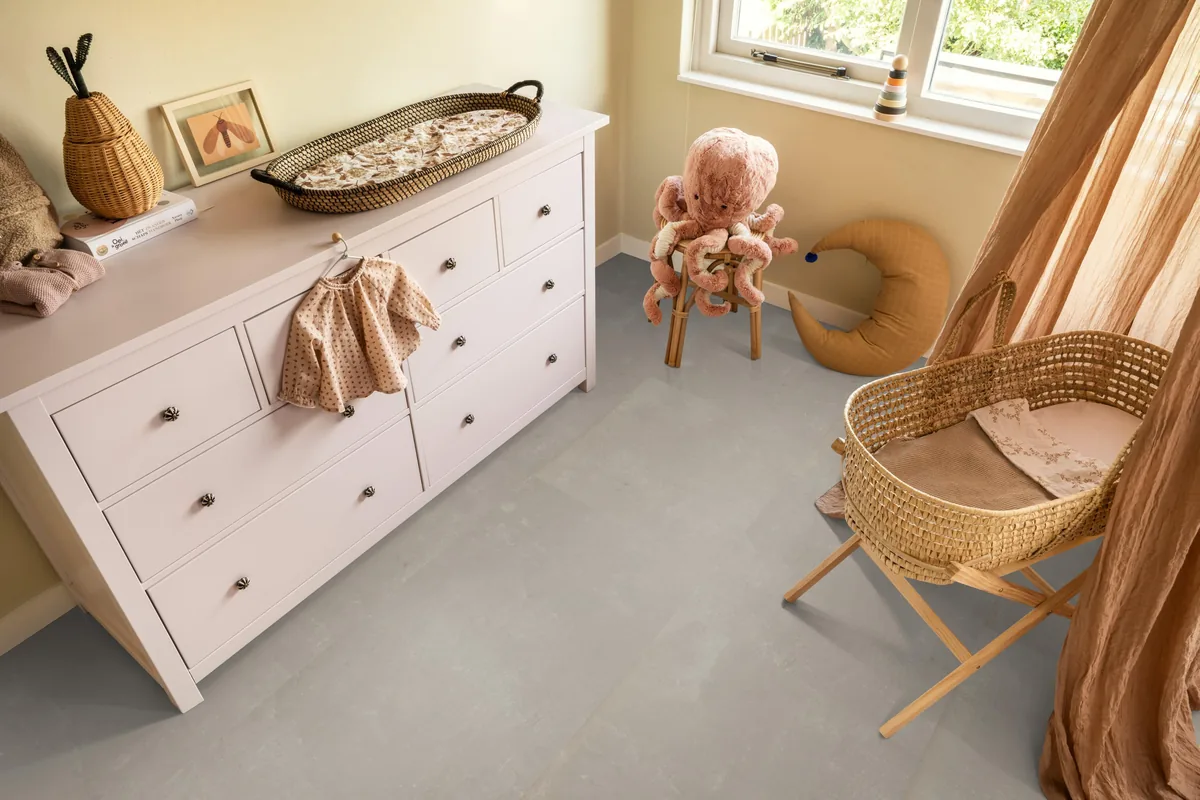 Westminster / Piero beige, klik pvc in een babykamer, met een witte commode en een rieten wieg