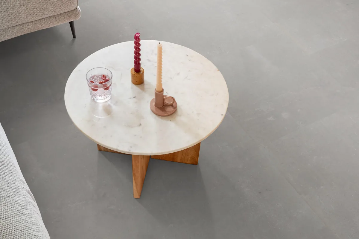 Westminster / Piero light grey, klik pvc in een woonkamer, met een ronde marmeren salontafel en twee kaarsen