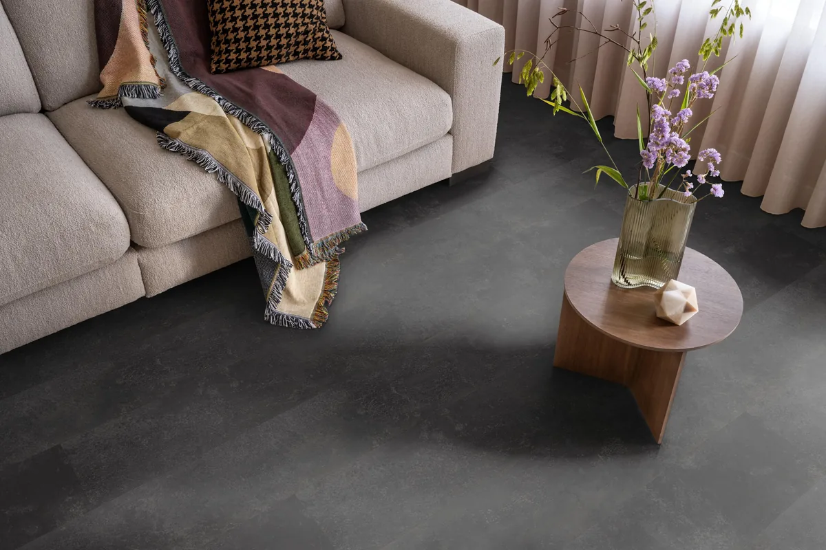 Finsbury / Viretto Anthracite, plak pvc in een woonkamer, met een beige bank en een ronde bijzettafel met bloemen
