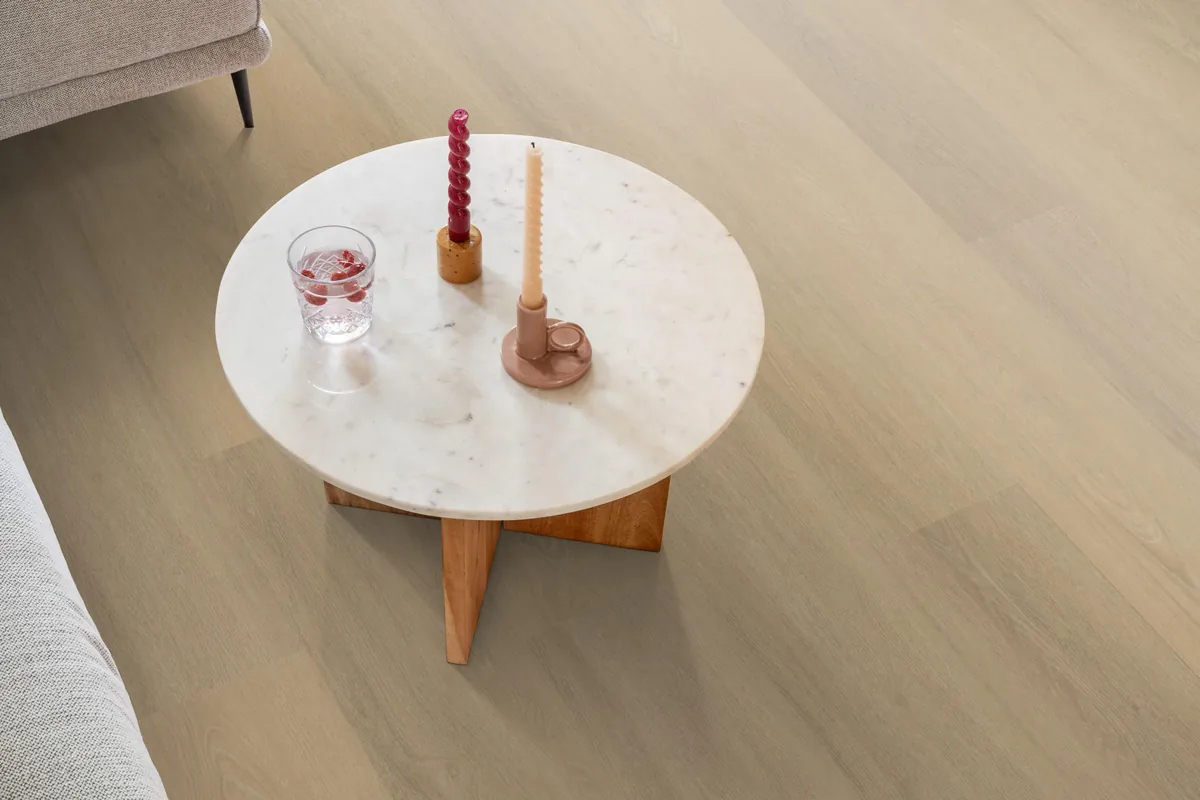 Sutton / Viranto Warm beige, klik pvc in een woonkamer, met een ronde marmeren salontafel en twee kaarsen