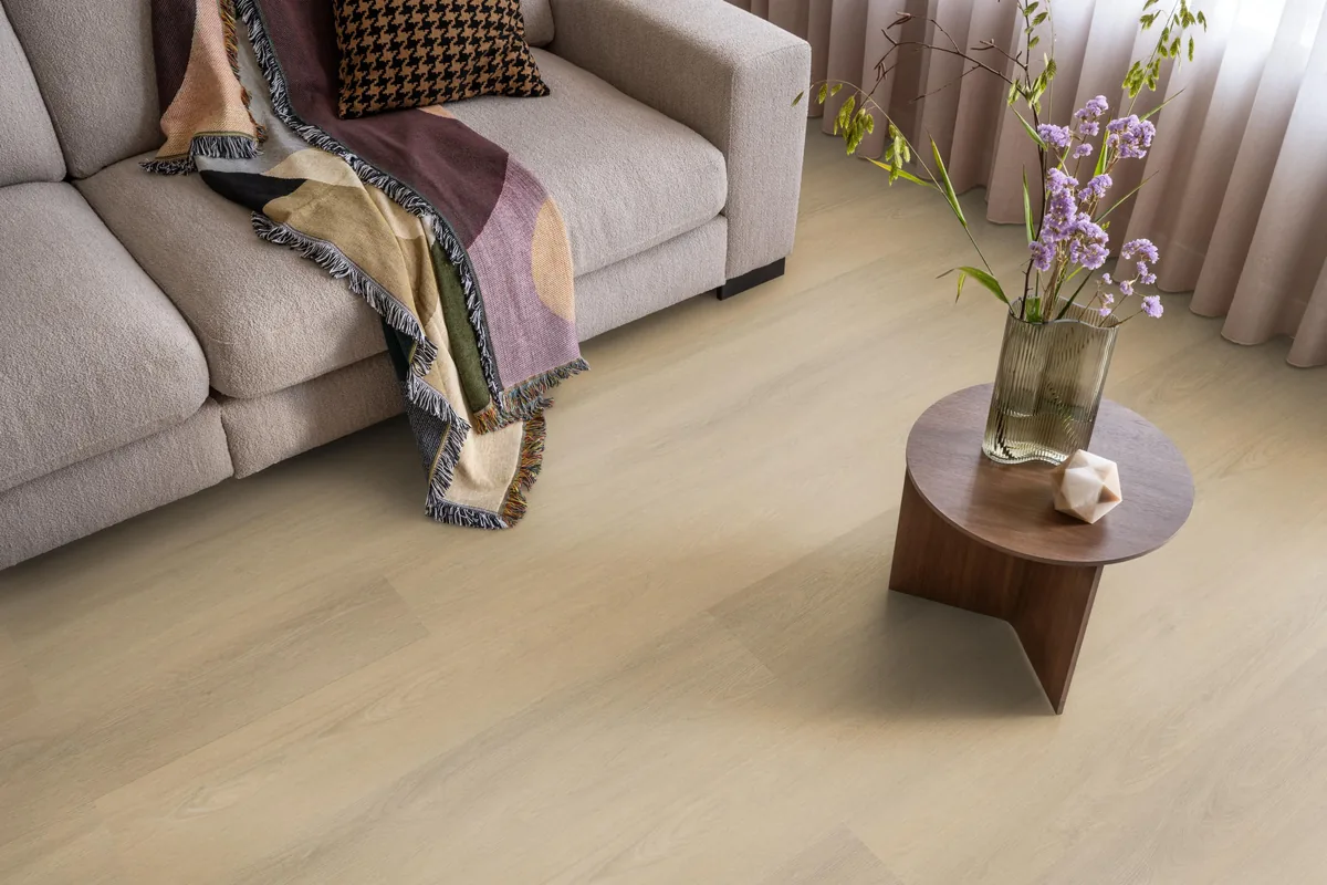 Sutton / Viranto Warm beige, klik pvc in een woonkamer, met een beige bank en een ronde bijzettafel met bloemen